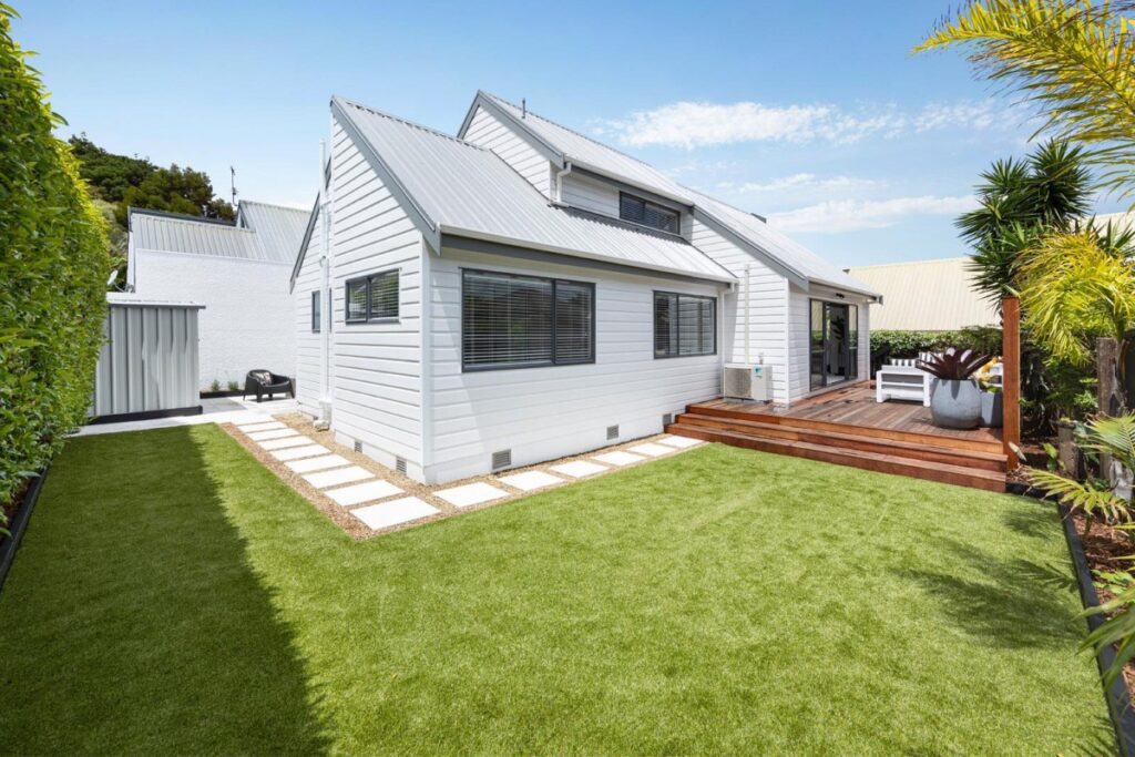 Tiling and turf combination: Modern white house with a green lawn and wooden deck, showcasing outdoor living and landscaping.