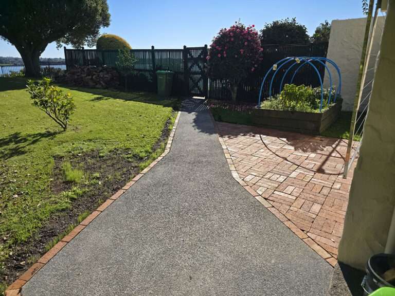 Brick pathway and pad showcasing landscape design with brick edging, garden, and fence, creating an inviting outdoor space.