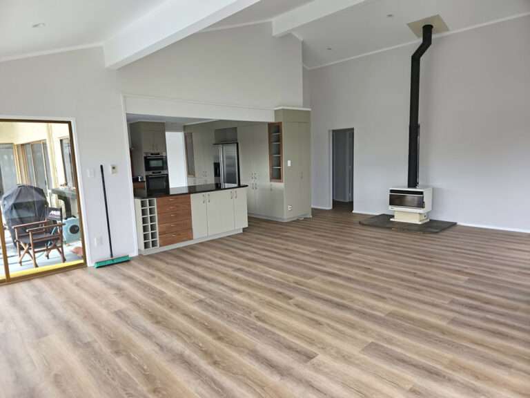 Newly painted open-plan living area featuring wood-look flooring, modern kitchen, and a freestanding fireplace. Fresh interior paint.
