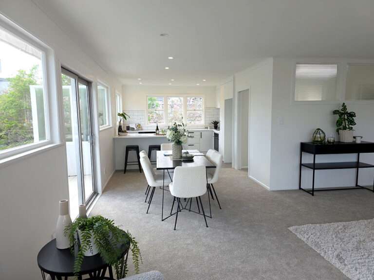 Bright, open-plan home interior with dining table, modern kitchen, and large windows. Fresh, renovated living space.