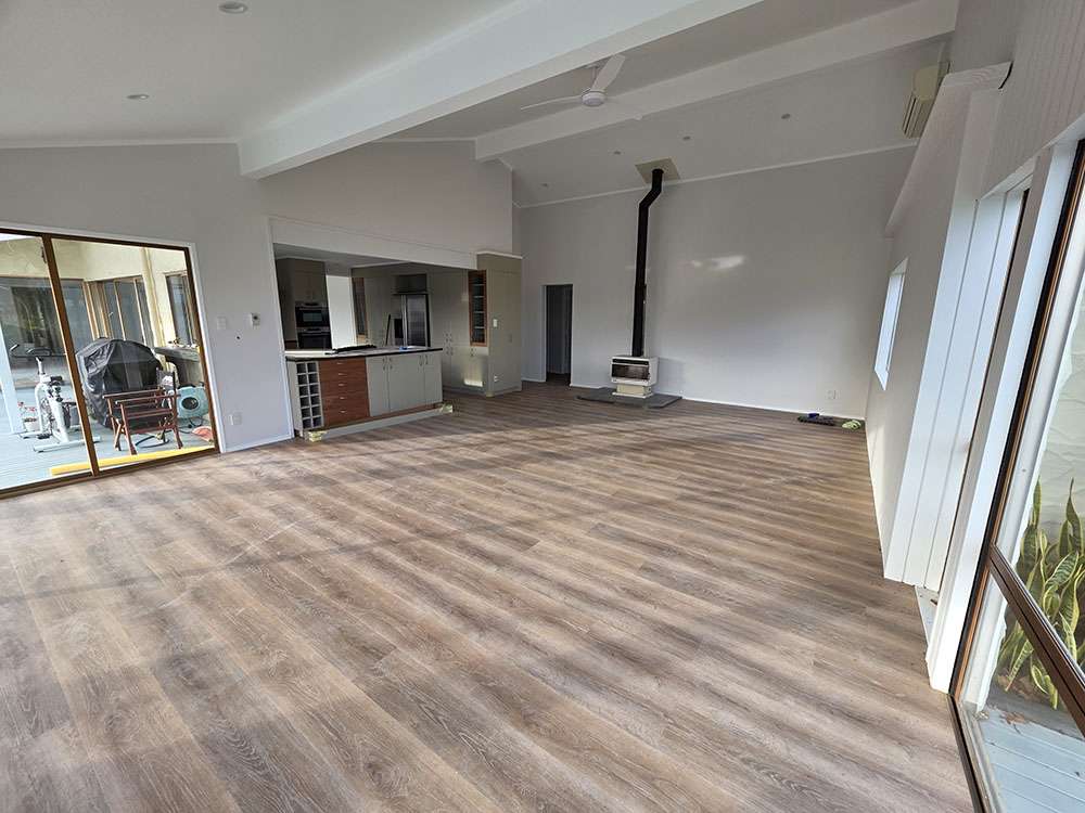 Spacious room featuring Lemonade flooring, open kitchen, fireplace, and large windows for a bright, modern interior.