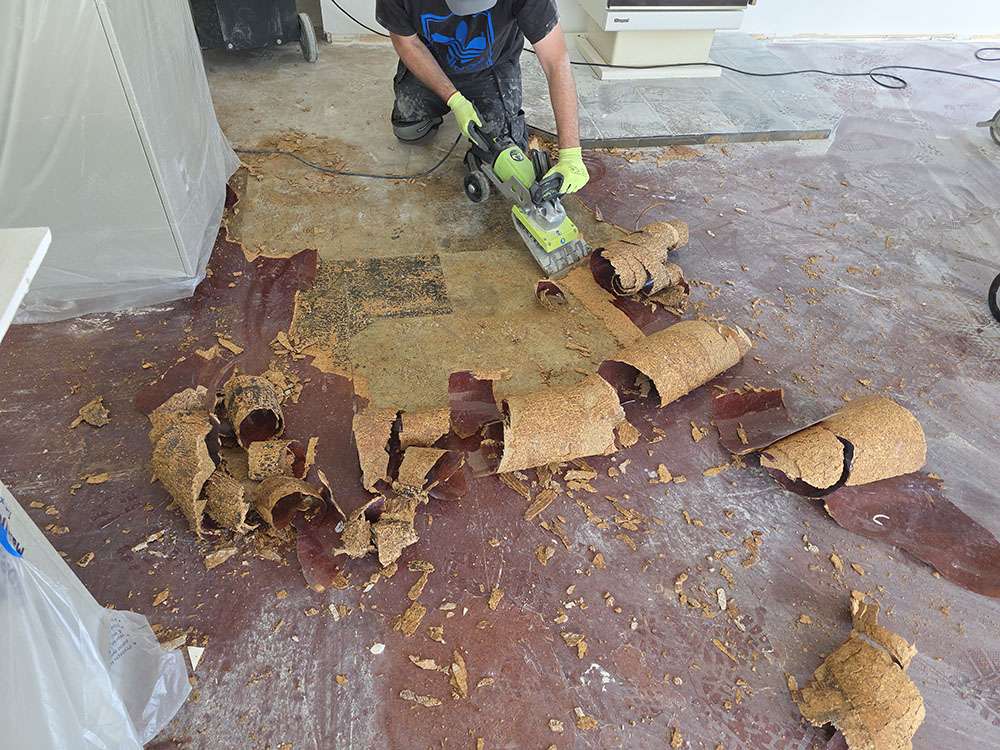 Man removing old flooring with a power scraper. Flooring renovation, floor removal, home improvement project.