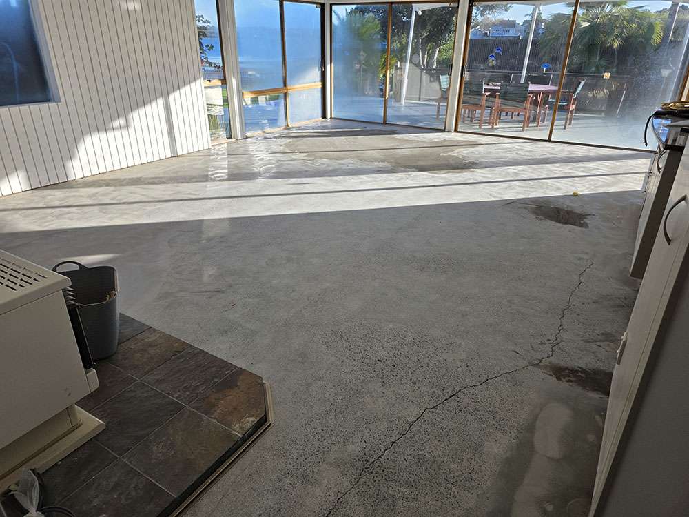 Polished concrete flooring in a sunroom with large windows, reflecting outdoor furniture and light, showcasing modern flooring design.