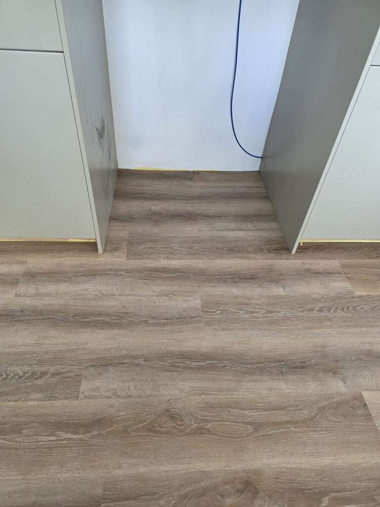 Close-up of light brown wood-look laminate flooring, installed beneath white cabinets, showcasing modern flooring design.