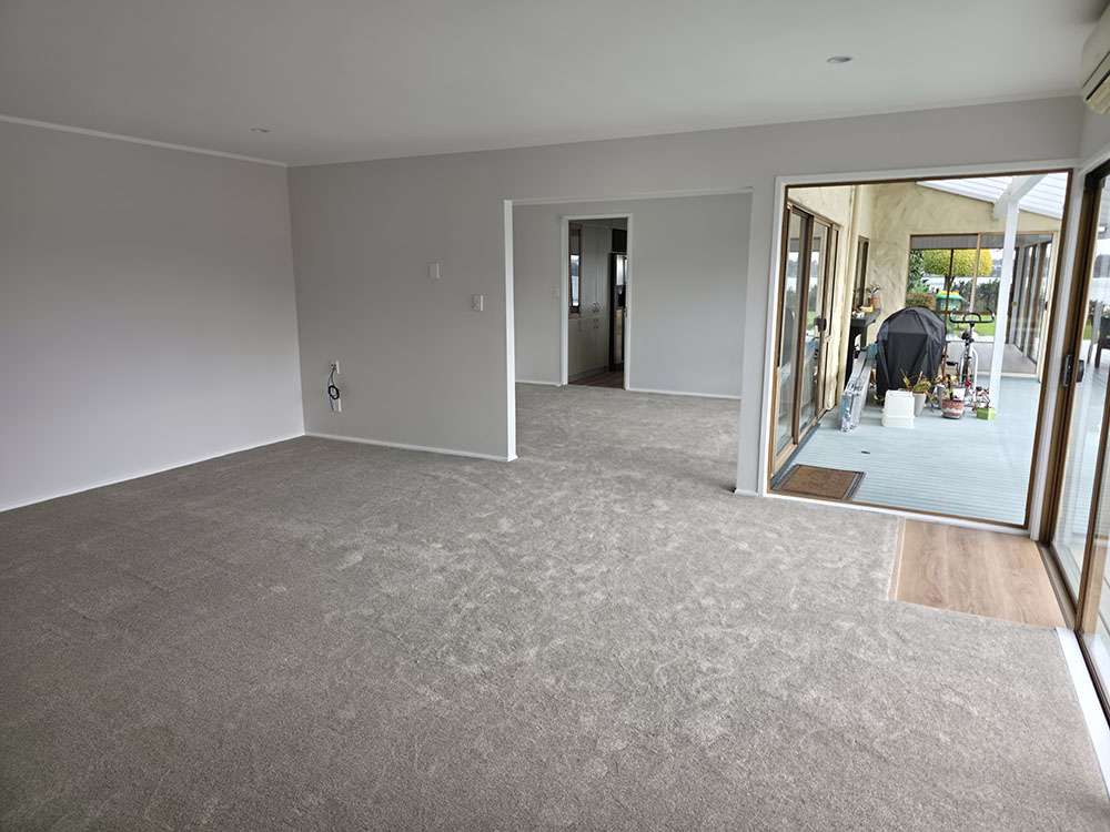 Newly installed gray carpet in a bright, modern living room with an open floor plan and sliding glass doors. New Carpet.