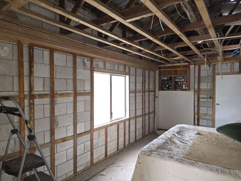 Unfinished room interior with exposed electrical box, concrete block walls, wood framing, and ladder. Renovation project.