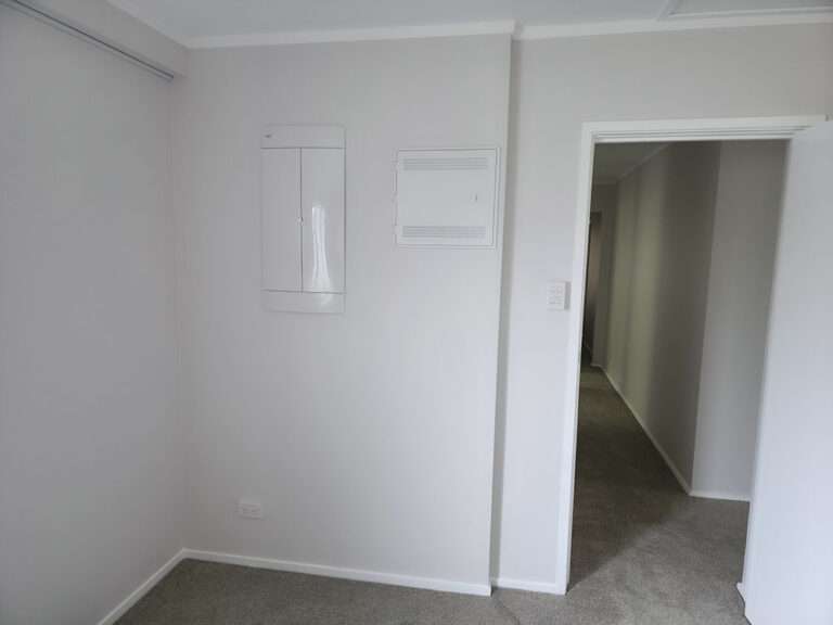 Interior view of a room featuring a new electrical box and access panel on a white wall, next to a doorway.