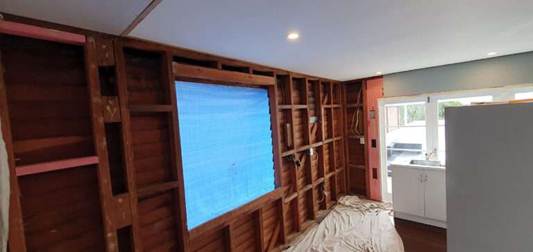 New kitchen renovation in progress, exposed studs and beams, blue tarp covering window, remodel construction site.