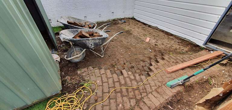 Outdoor tiling project in progress: wheelbarrows with bricks, brick patio, building materials.