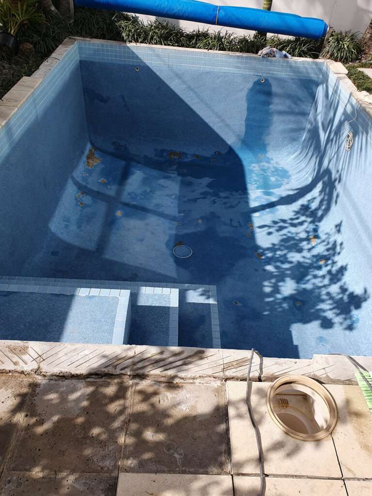 Empty swimming pool needing painting and renovation. Blue tiled pool with steps and cover, ready for a fresh coat of paint.