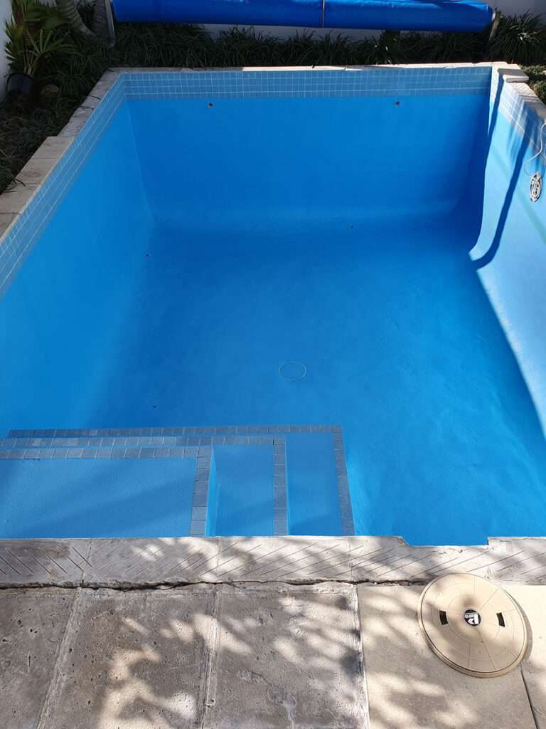Freshly painted swimming pool with bright blue paint, tiled steps, and clean pool deck. Pool renovation project.