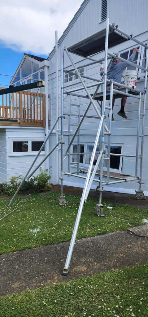 Scaffolding system used for house painting. Painter on scaffolding working on a white two-story house in a case study.