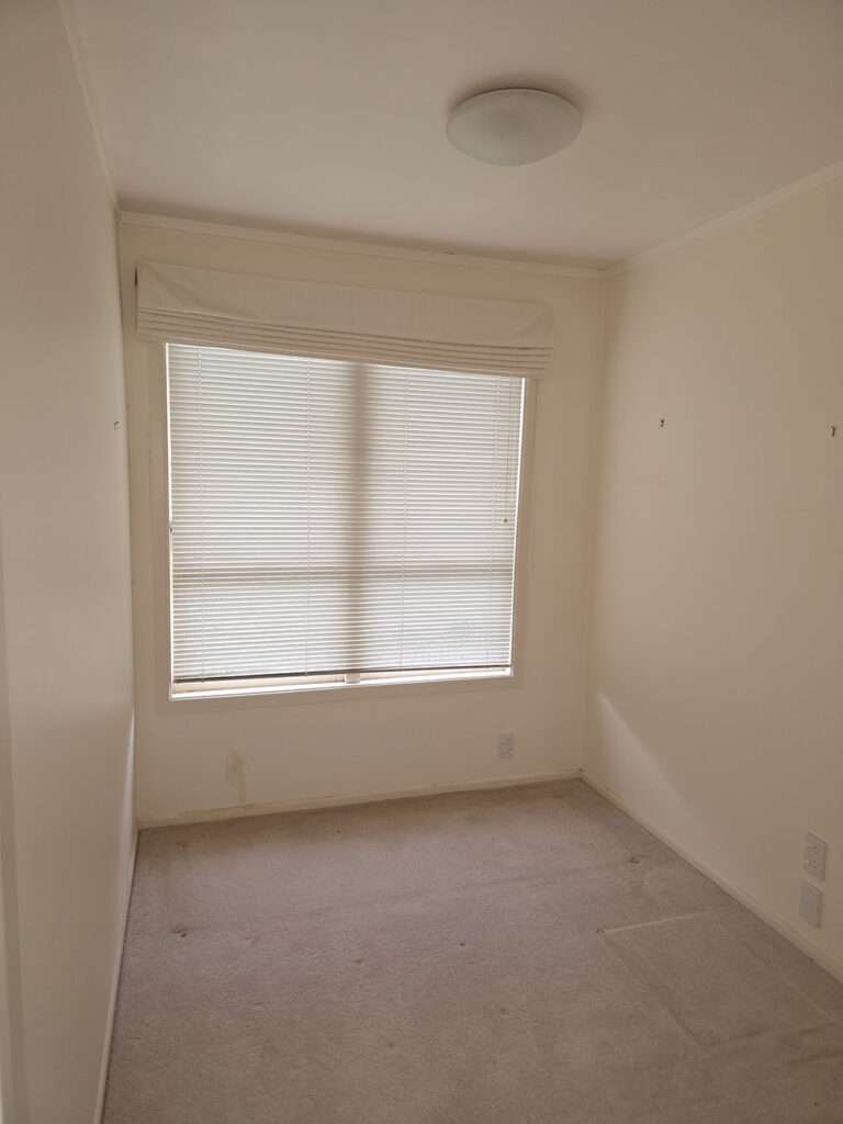 Small, empty bedroom interior with carpet, window with blinds, and a ceiling light fixture. Ready for room staging.