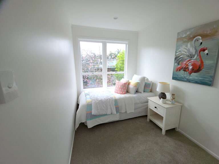 Cozy single bedroom with bed near window, flamingo art, and white nightstand. Small room interior design.