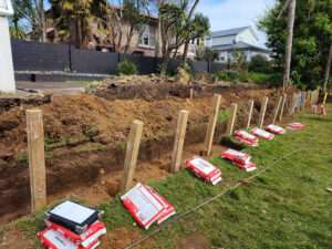 Garden retaining fence construction: Wooden posts, bags of concrete mix ready for installation. Case study of garden project.