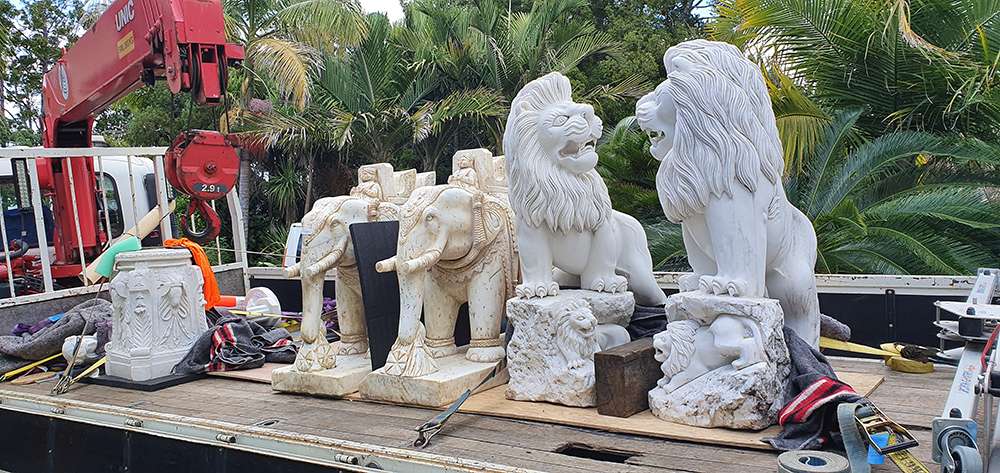 Hiab crane lifting ornate stone statues of lions and elephants off site. Moving heavy sculptures with lifting equipment.