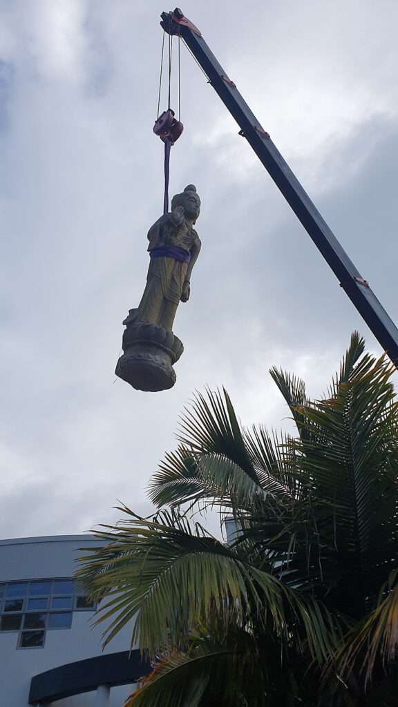 Hiab crane lifting stone Buddha statue off site. Heavy lifting equipment in action, case study on display.