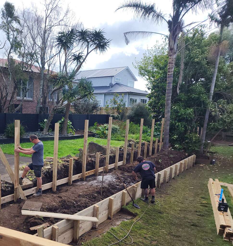 Garden retaining fence construction in progress. Wooden structure and supporting posts being built for landscaping project.