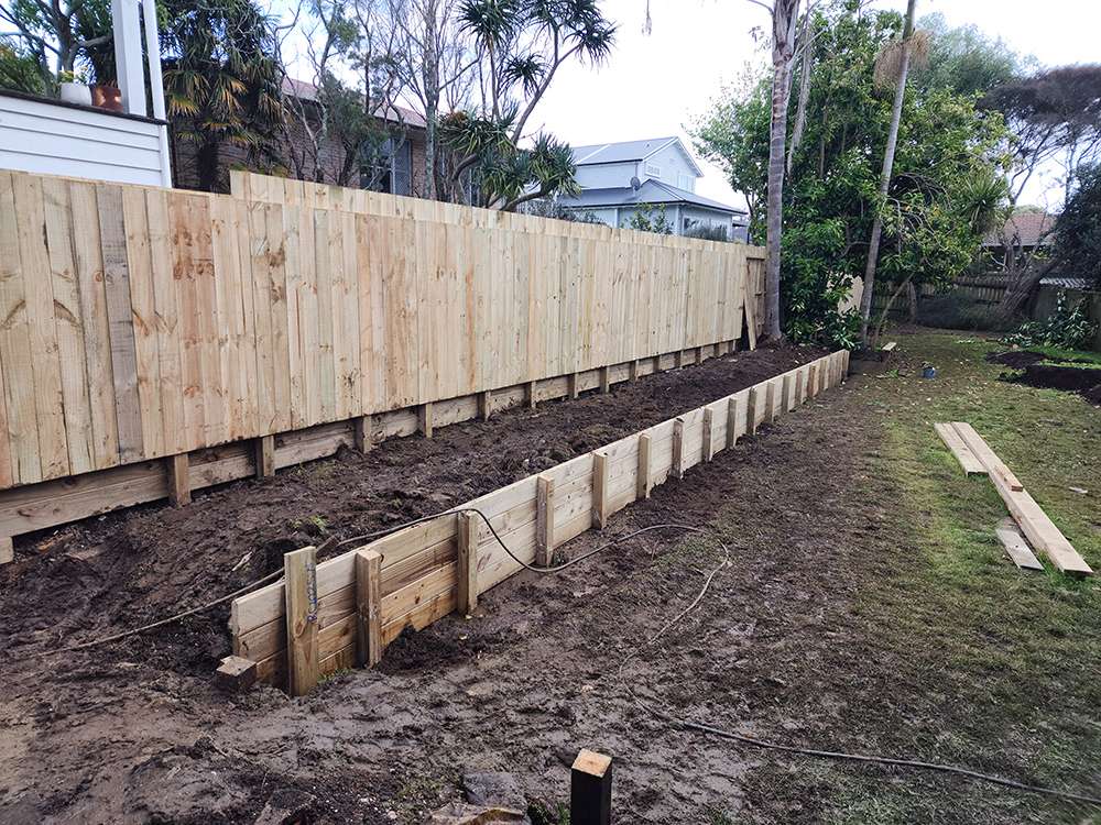 New wooden garden retaining fence installed, showcasing a sturdy timber structure for soil retention and garden design.