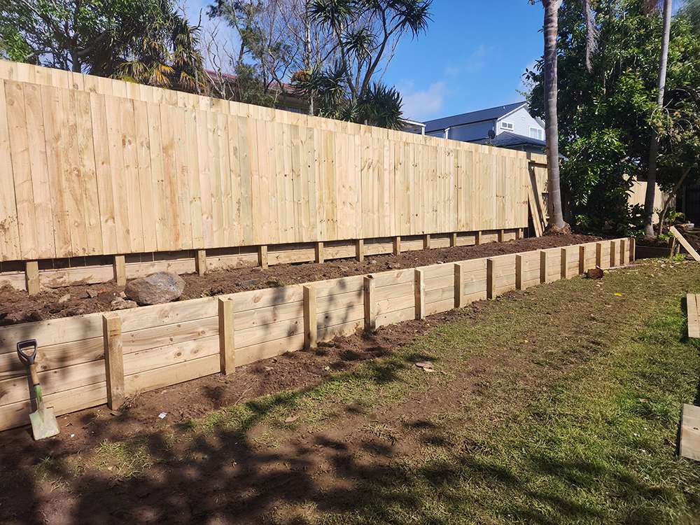 Garden retaining fence case study. Timber retaining wall and wooden fence on a grassy lawn.