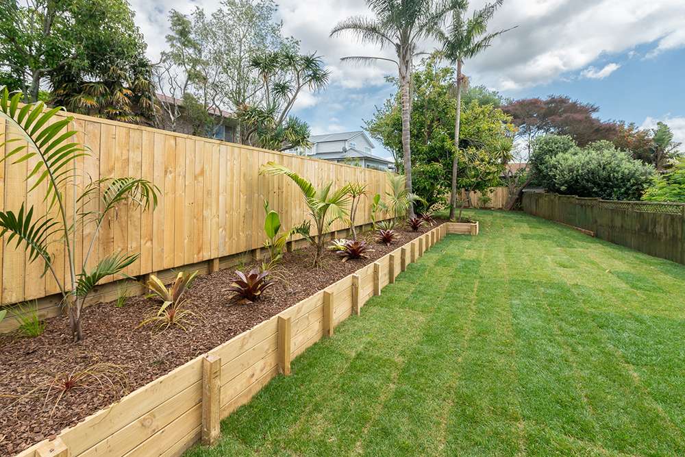 Landscaped backyard with vibrant green lawn, wooden fence, garden bed, and tropical plants. Ideal for outdoor living.
