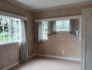 Interior wall insulation project: Empty room showing walls before insulation, windows with curtains, light brown carpet.