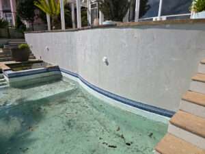 Exterior concrete resurfacing case study: Dirty swimming pool with damaged concrete wall before renovation.
