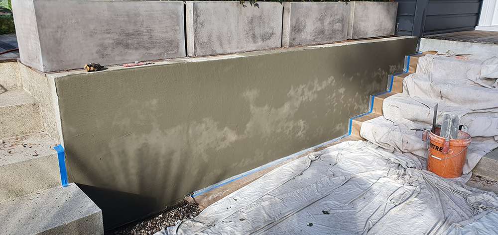 Exterior concrete resurfacing project showing newly applied concrete on a retaining wall and stairs, with tools nearby.