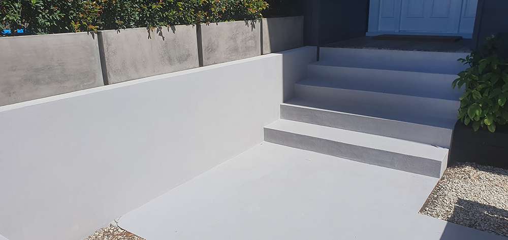 Exterior concrete resurfacing project showcasing a smooth, bright white finish on walls, steps, and ground surfaces.