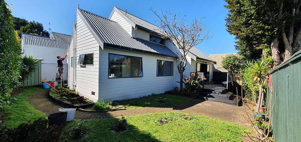 Kwila decking repair case study: Exterior view of a house with a worker on a ladder.