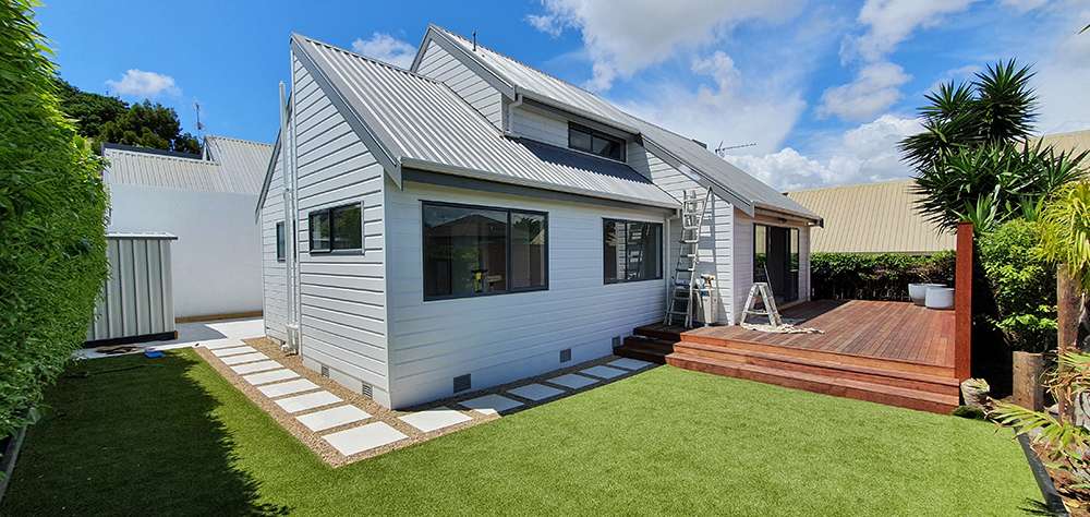 Kwila decking repair project: Modern home exterior with a newly renovated wooden deck and green lawn. Decking looks clean and restored.