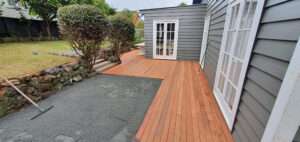 Kwila decking repair project. New hardwood deck installation adjacent to a gray, shingle-style house with white trim.