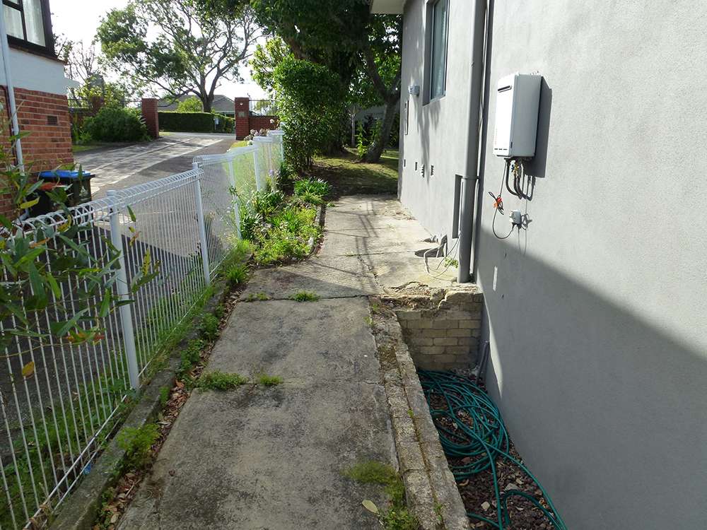 Kwila decking repair case study: Concrete path alongside building with white fence, emphasizing outdoor renovation and maintenance.
