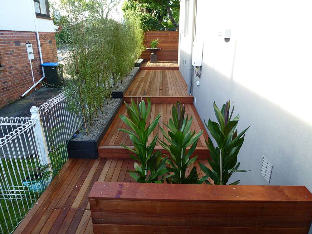 Kwila decking repair case study: View of a beautifully restored wooden deck with plants and greenery.