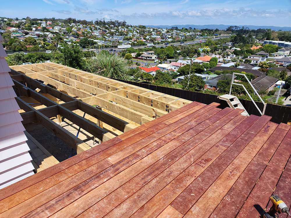 Kwila decking repair case study. Half-finished wooden deck with timber beams and reddish-brown planks overlooking a town.