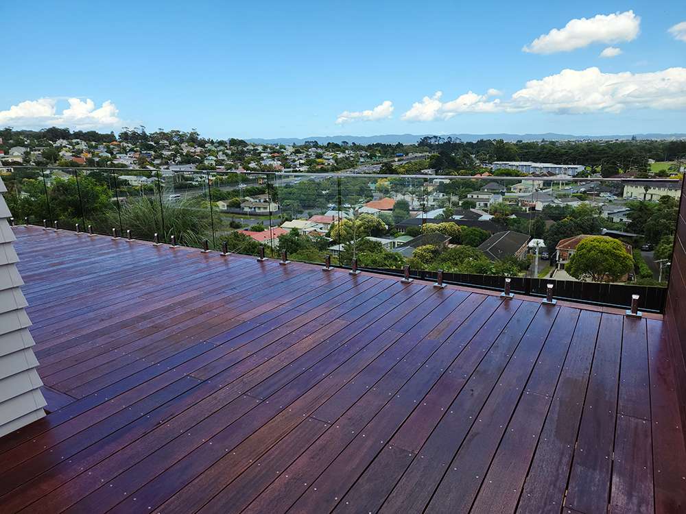 Kwila decking repair case study: a refurbished timber deck with glass balustrade overlooking a suburban landscape.