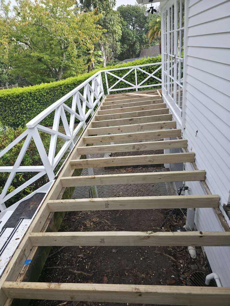 Kwila Decking Repair: Wooden frame of a deck under construction with white railings and steps leading to a white house.