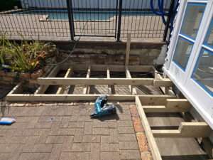 Building a decking handrail: Timber framework construction with a nail gun, showing the initial stages of deck installation.