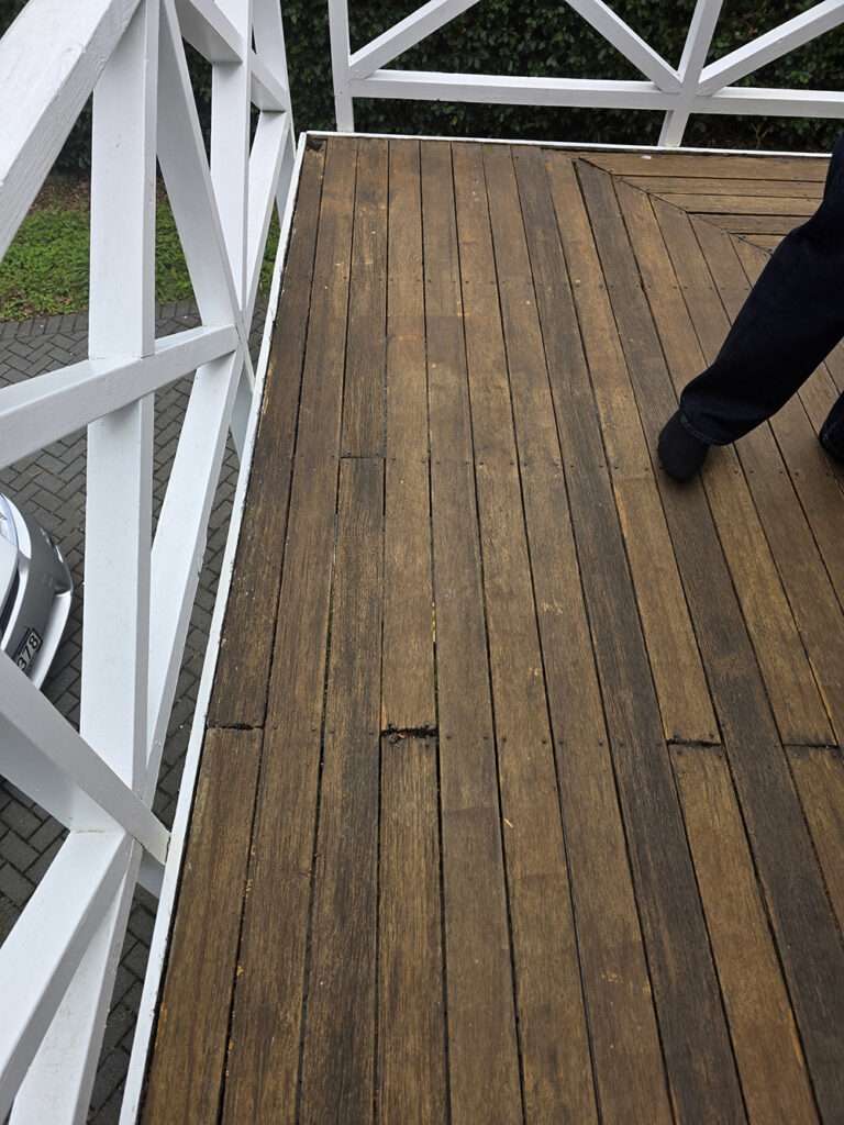 Rotten timber decking used as a handrail, showcasing damaged wood planks and white railing structure in a case study.