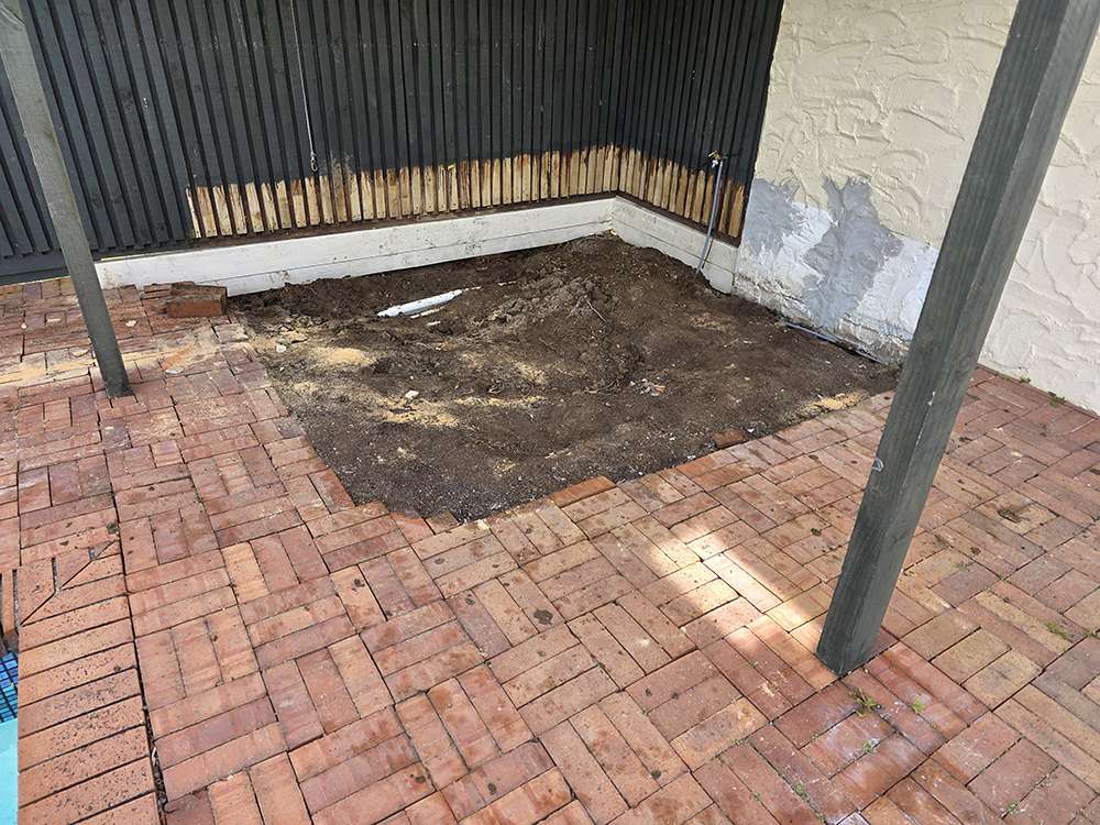 Brick releveling project: Uneven patio bricks, dirt patch, and foundation work. Home improvement case study.