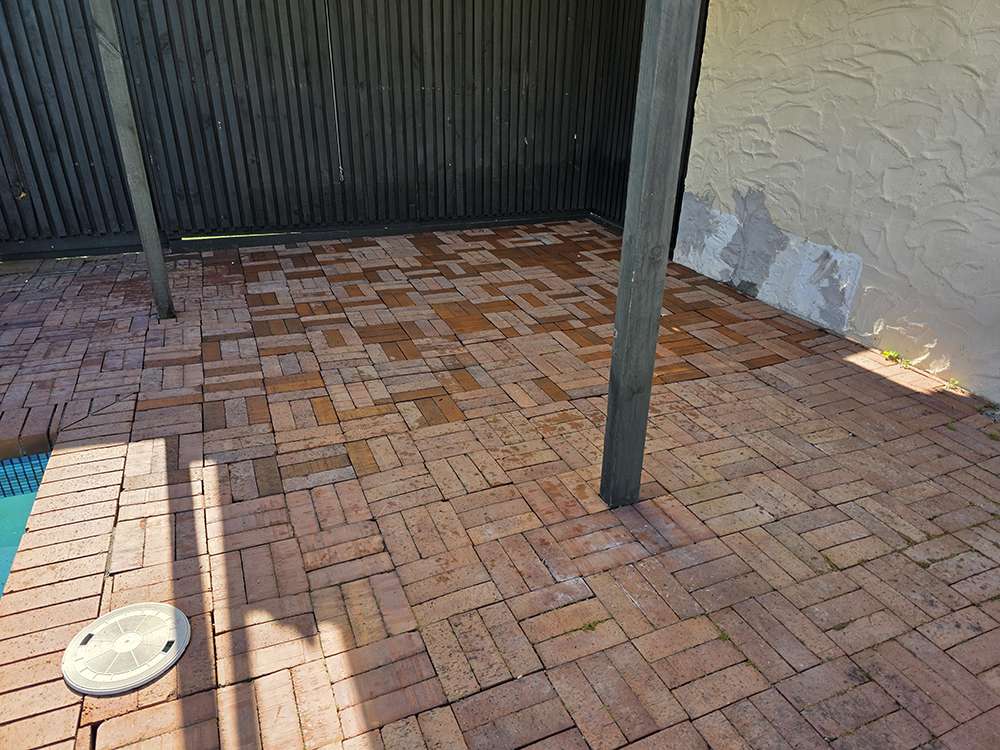 Brick Releveling Case Study: Releveled brick patio surface with herringbone pattern, adjacent to a pool and fence.