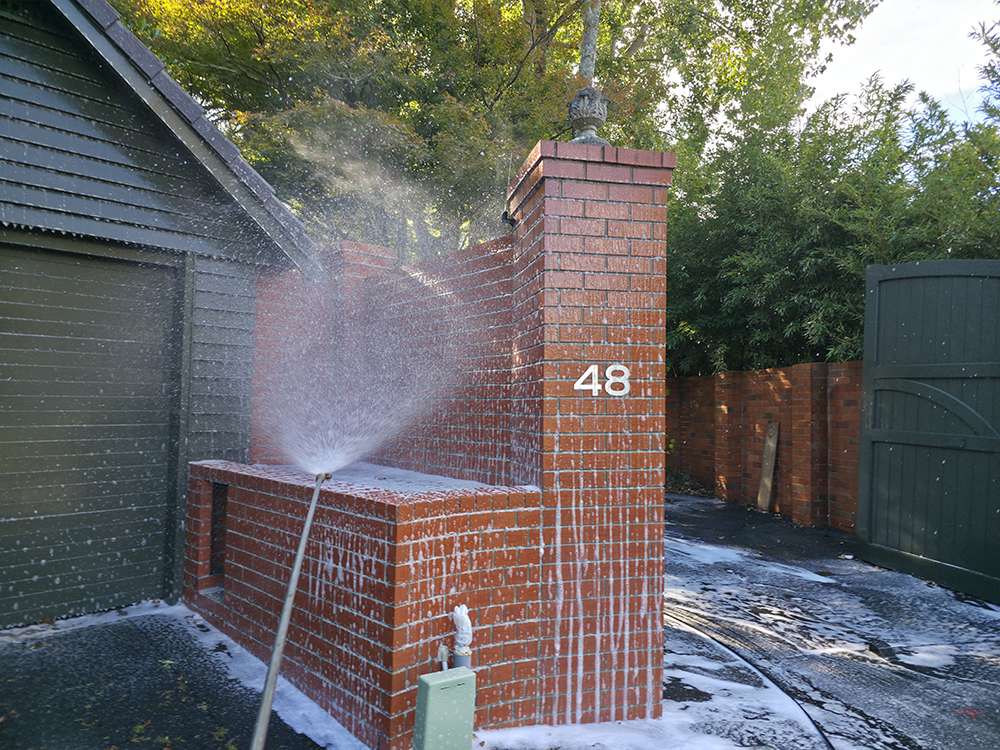 Moss & Mould treatment: Brick wall being pressure washed for moss and mould removal on residential property, number 48 visible.