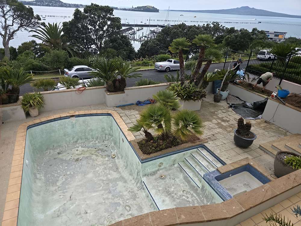 Pool painting preparation; empty swimming pool awaiting painting and pump repair, with garden and coastal view in the background.