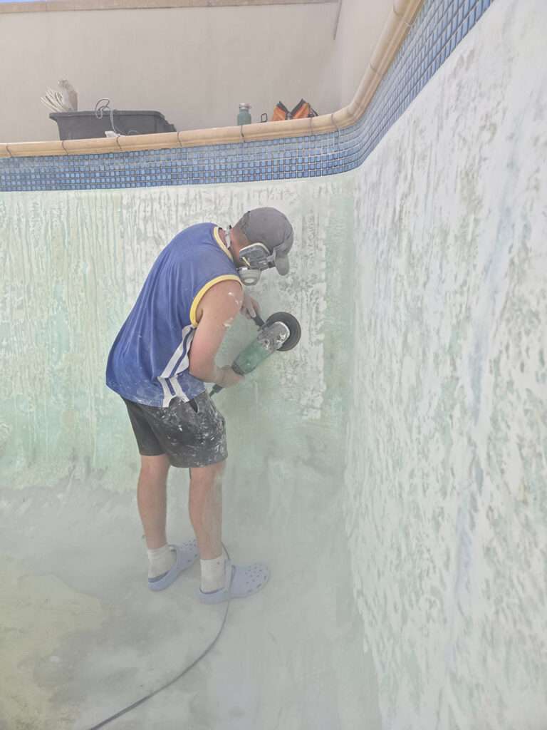 Pool painting: Man grinding pool wall in preparation for new paint. Pool repair and renovation project.