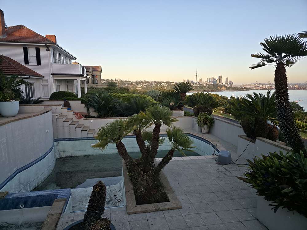 Pool painting project. Empty swimming pool ready for painting and pump repair with Auckland city skyline in the background.